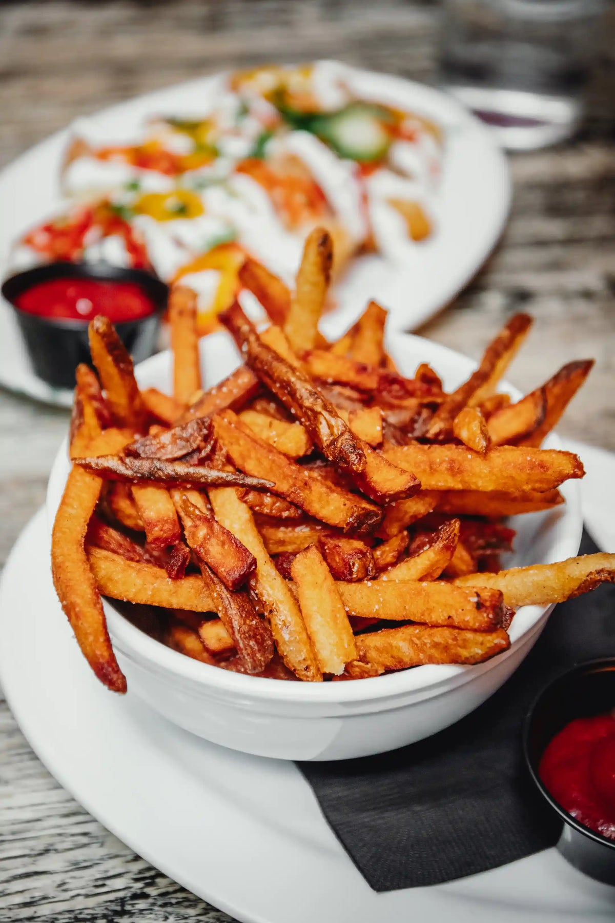 Bowl of crispy fries with ketchup on a wooden table