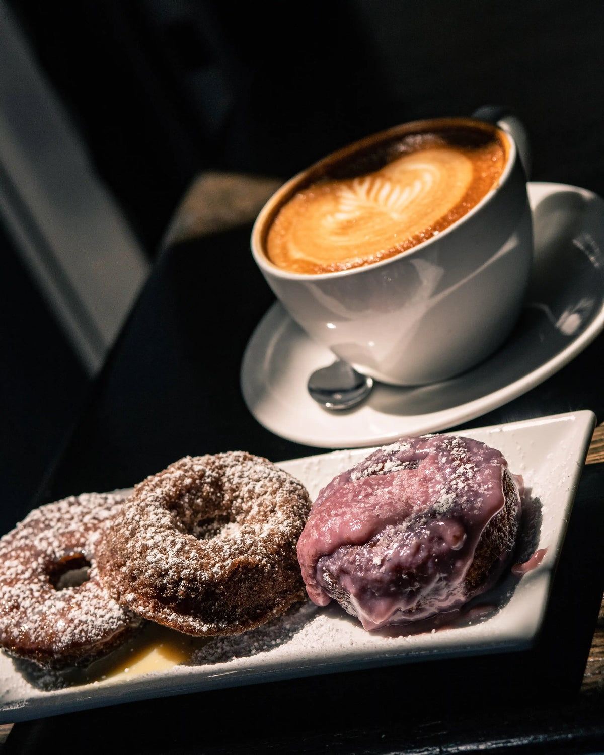 Three donuts on a plate with a cup of Bean2Bean coffee in the background