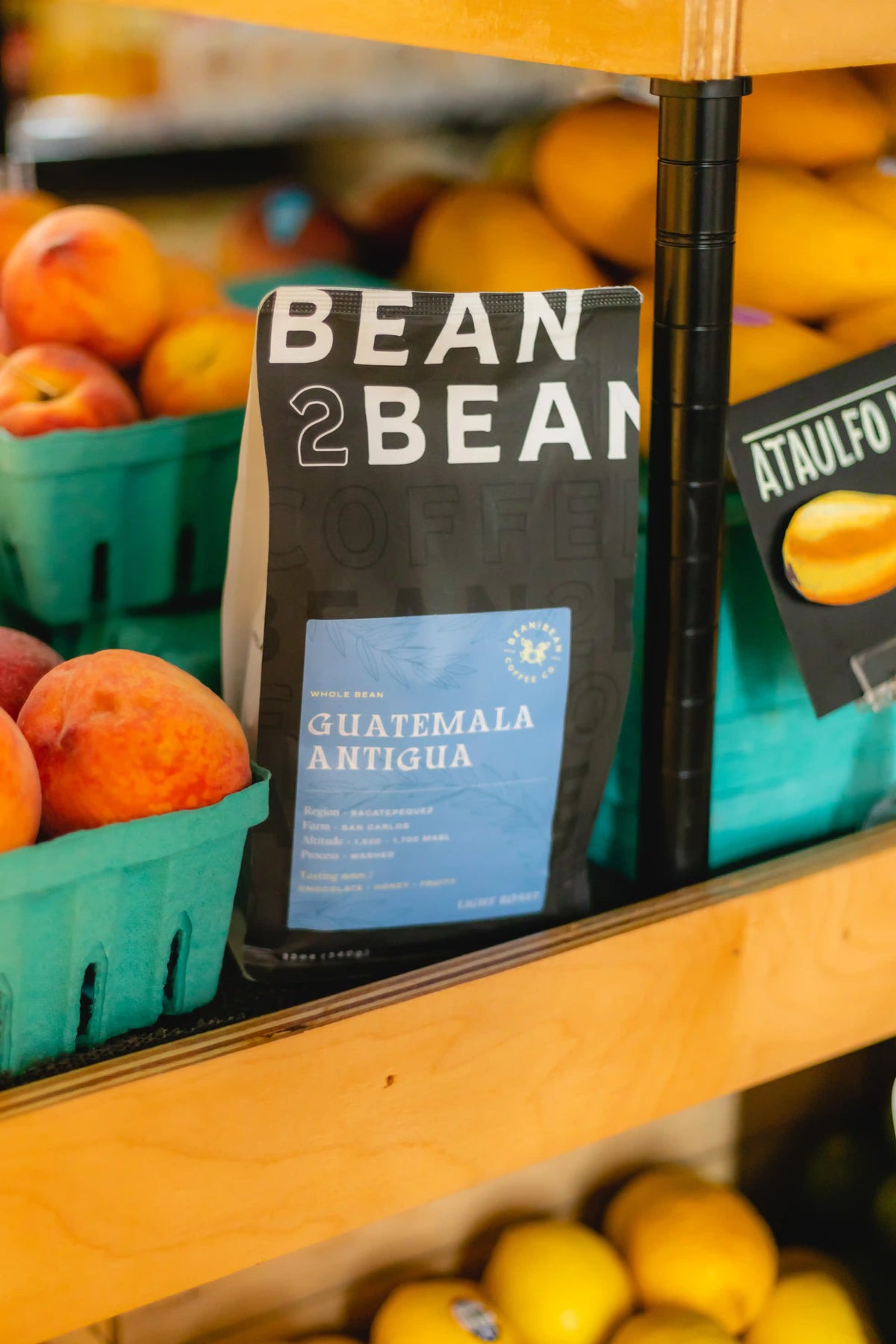 Bean to Bean Guatemala Antigua coffee bag on a fruit shelf with peaches and lemons.