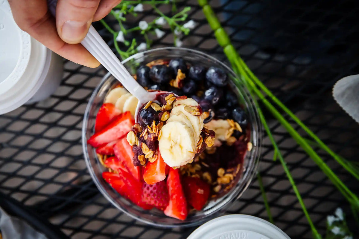 Spoonfull of fruit, oat, and banana over a blurred fruit cup from above