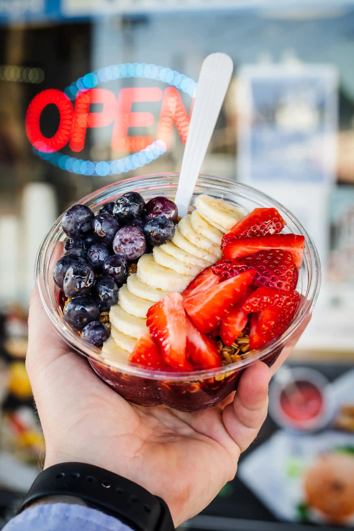 Person's and holding a fruit cup with bananas, strawberries, and blueberries visible