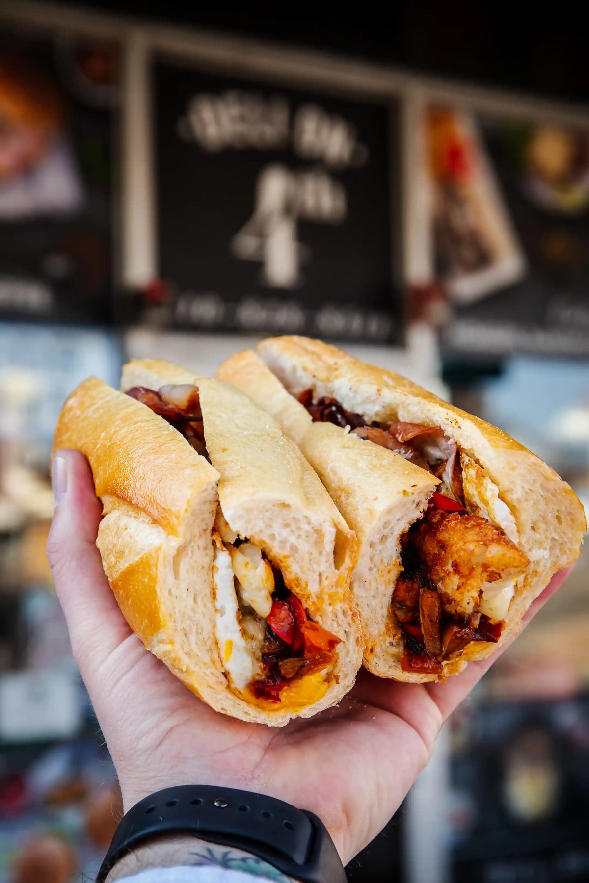 Person's hand holding a hashbrown and potato breakfast longroll sandwich