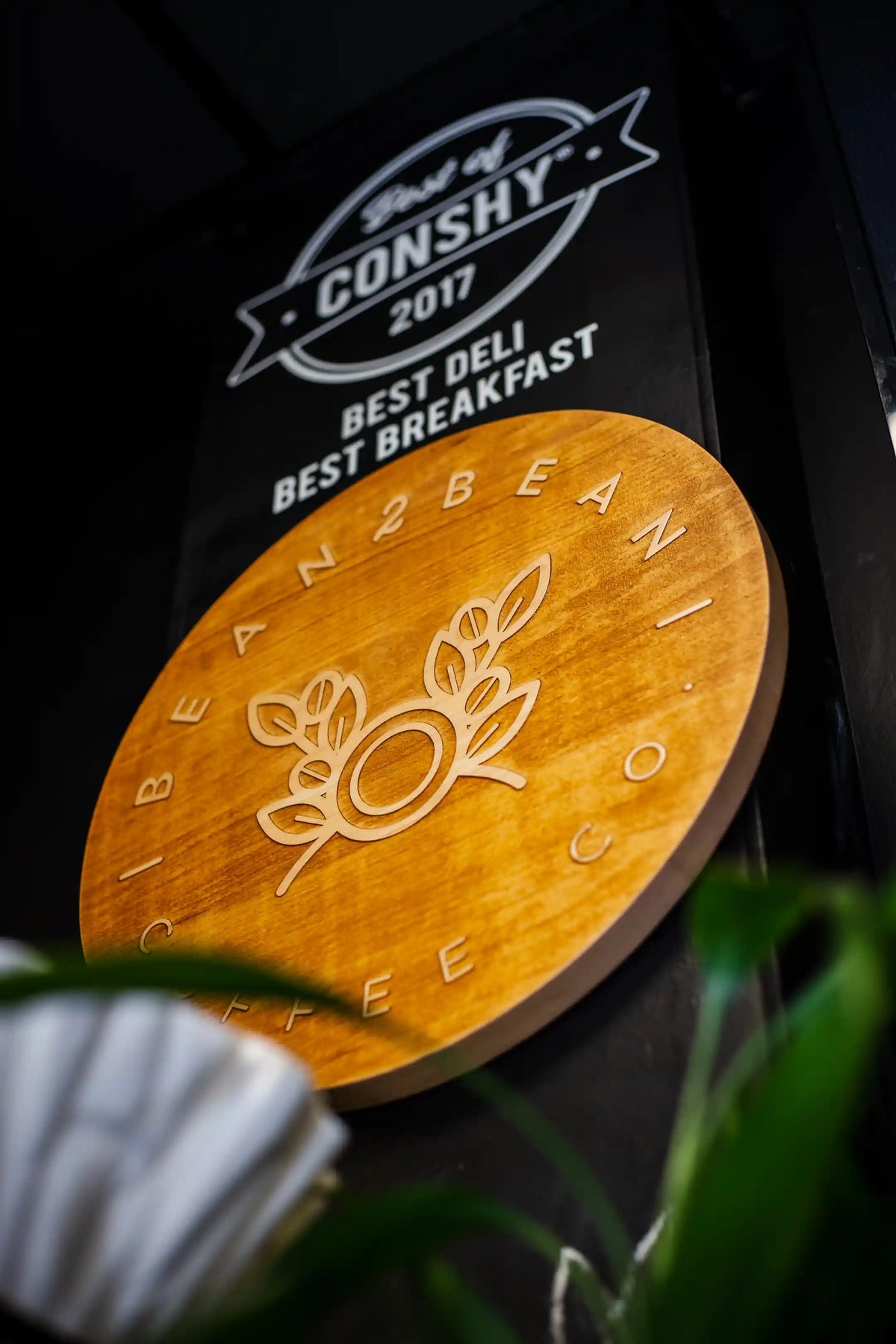 wooden round sign hanging on wall that says "Bean2Bean coffee co" around the edge with their logo in the center