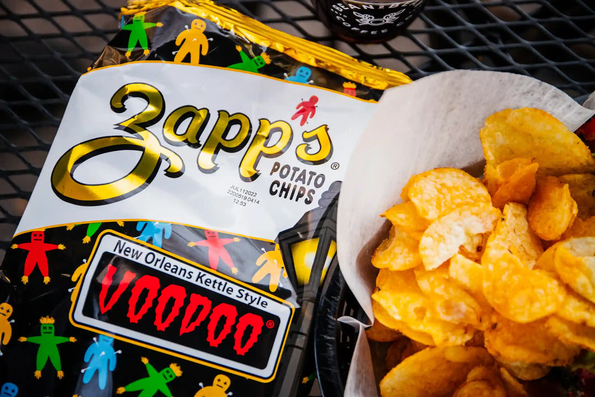Zapp's potato chips bag front next to chips in basket on black metal surface