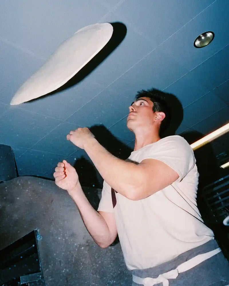 Person throwing pizza dough into the air in a kitchen setting