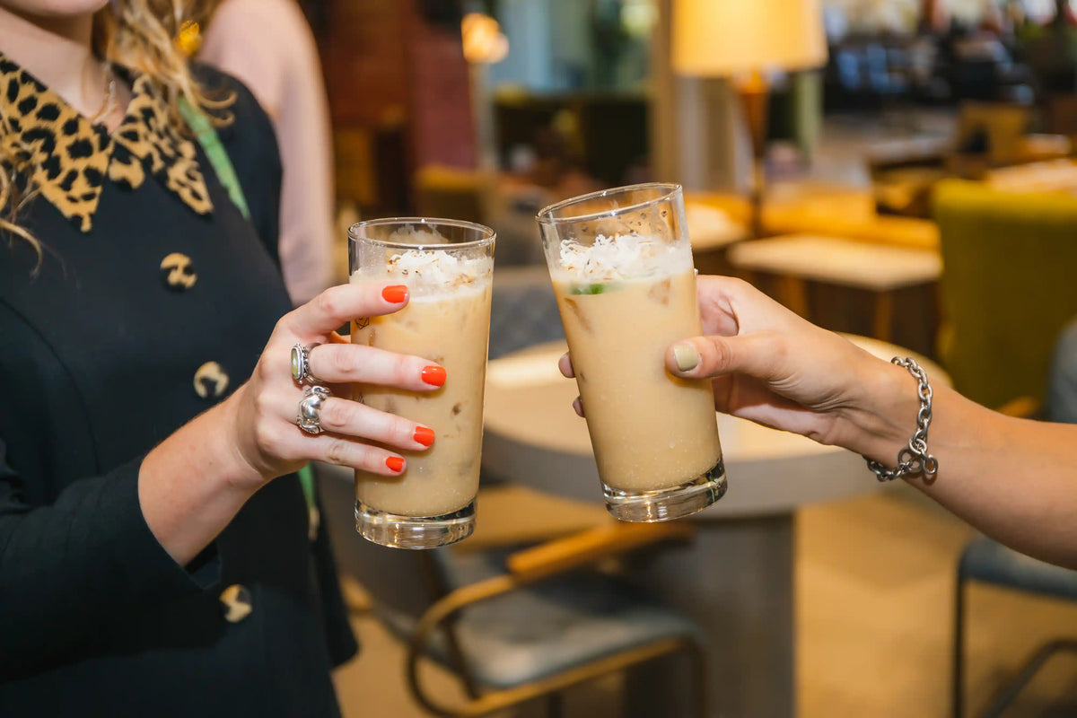 Two people clinking glasses of iced coconut cocktail in a casual setting