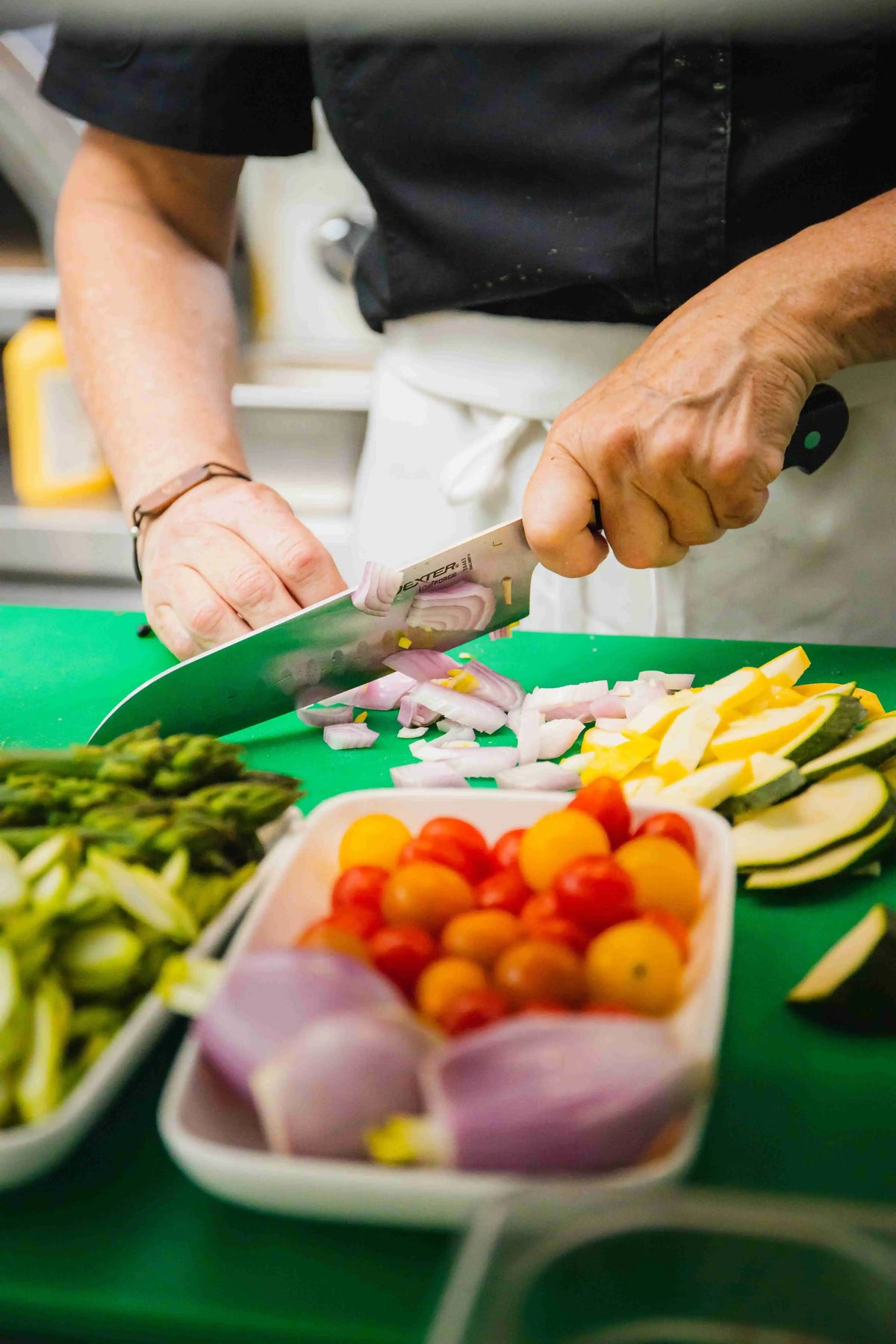 Chef prepping and cutting vegetables on a green cutting board