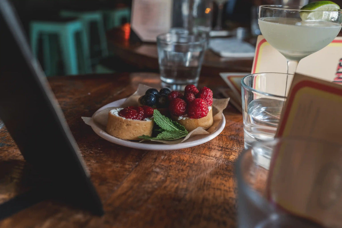 Berry shortcakes on a white plate garnished with mint on a wooden table with glasses and menus around