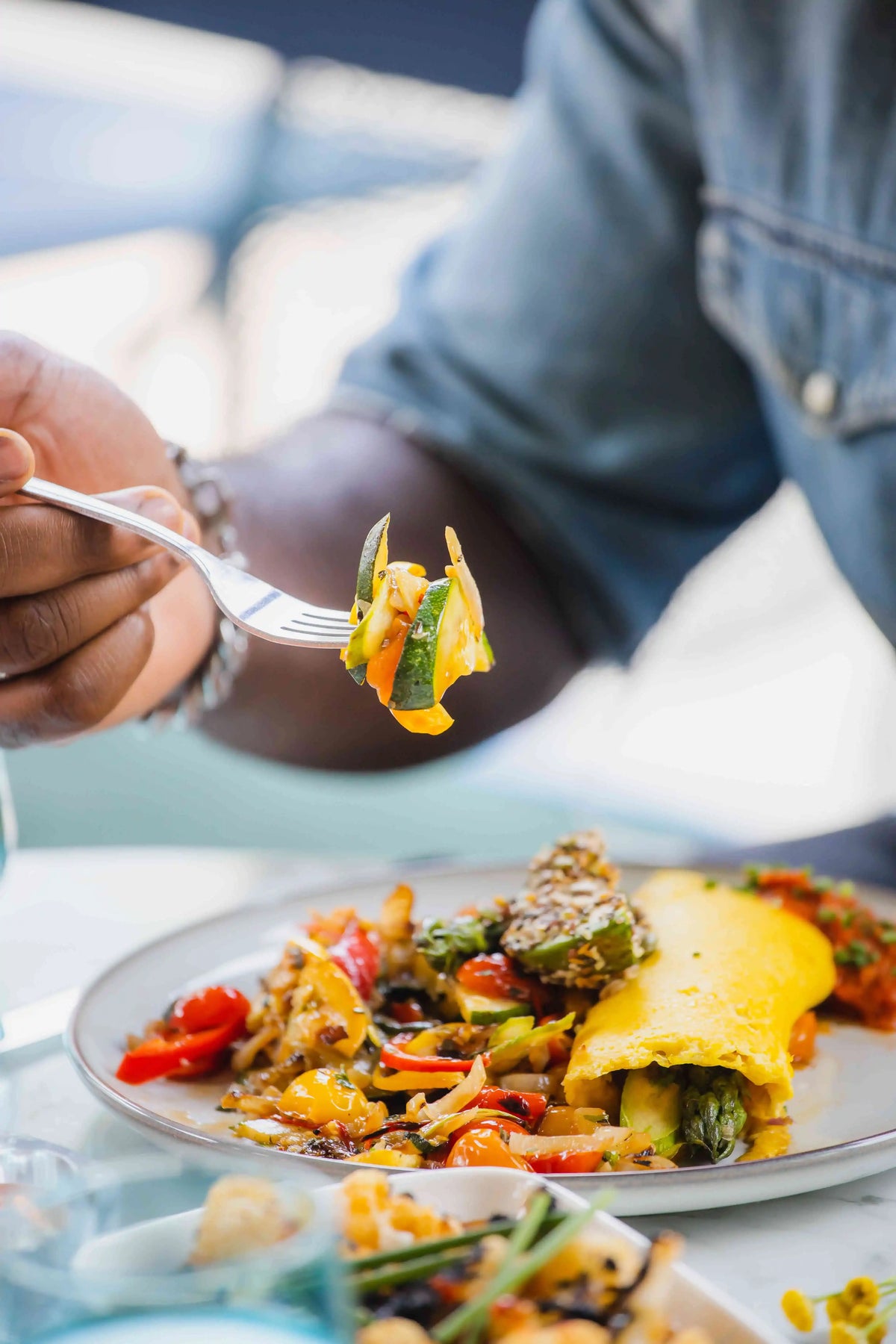 Person holding a fork with veggies on it from a veggie omelette on a plate