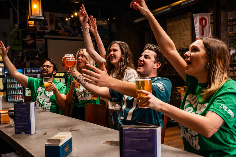 Group of people in green Philadelphia Eagles shirts celebrating with drinks in a bar.