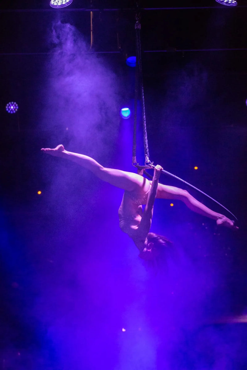 Aerialist performing on a rope against a dark background with purple lighting