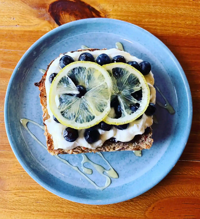 Toast with lemon slices, blueberries, and cream on a blue plate on a wooden table