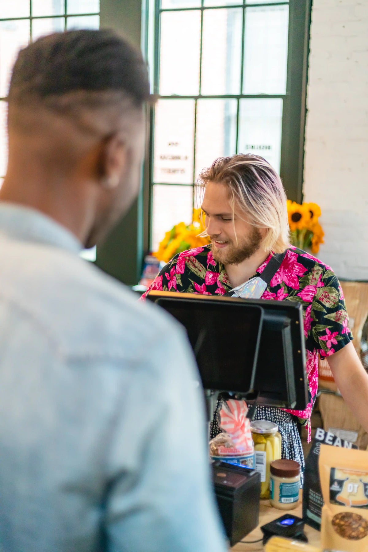 Person with blonde hair and floral shirt interacting with a cash register in a casual setting.