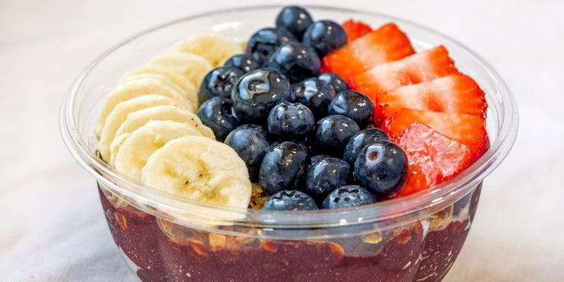 Fruit salad with blueberries, strawberries, and bananas in a clear container on a light background