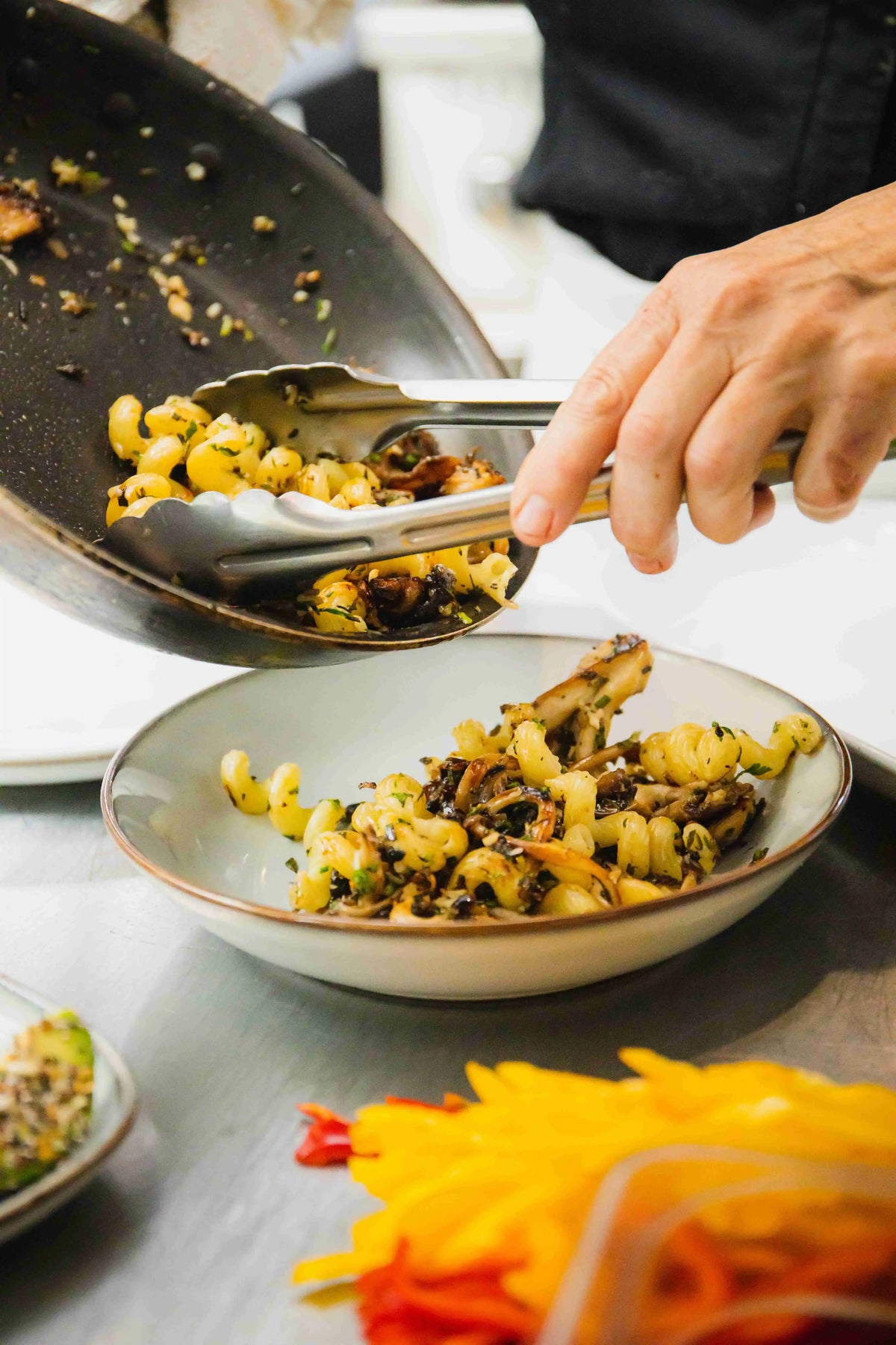 Mushroom noodle dish being served into bowl from pan with tongs by chef