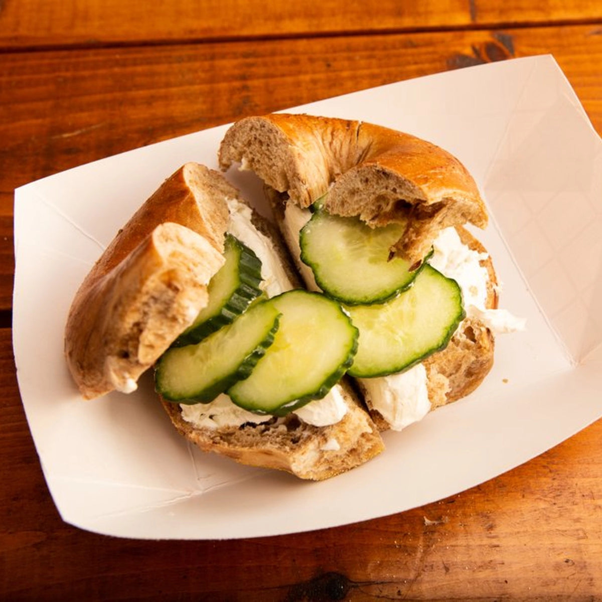 Bagel with cream cheese and cucumber slices on a wooden surface