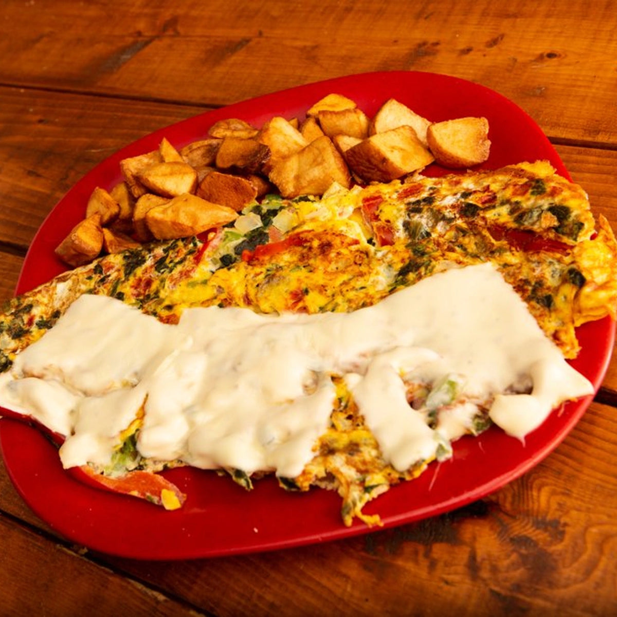 Omelette breakfast platter with various toppings and a side of homestyle potatoes on a wooden table.