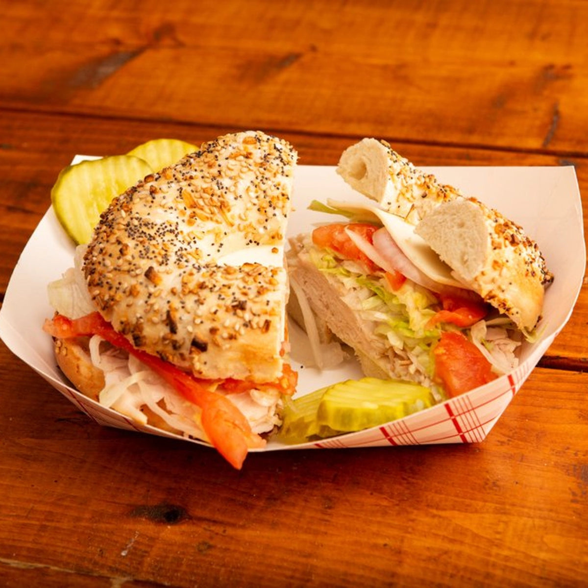 Bagel sandwich cut in half on a paper plate with pickles on a wooden table