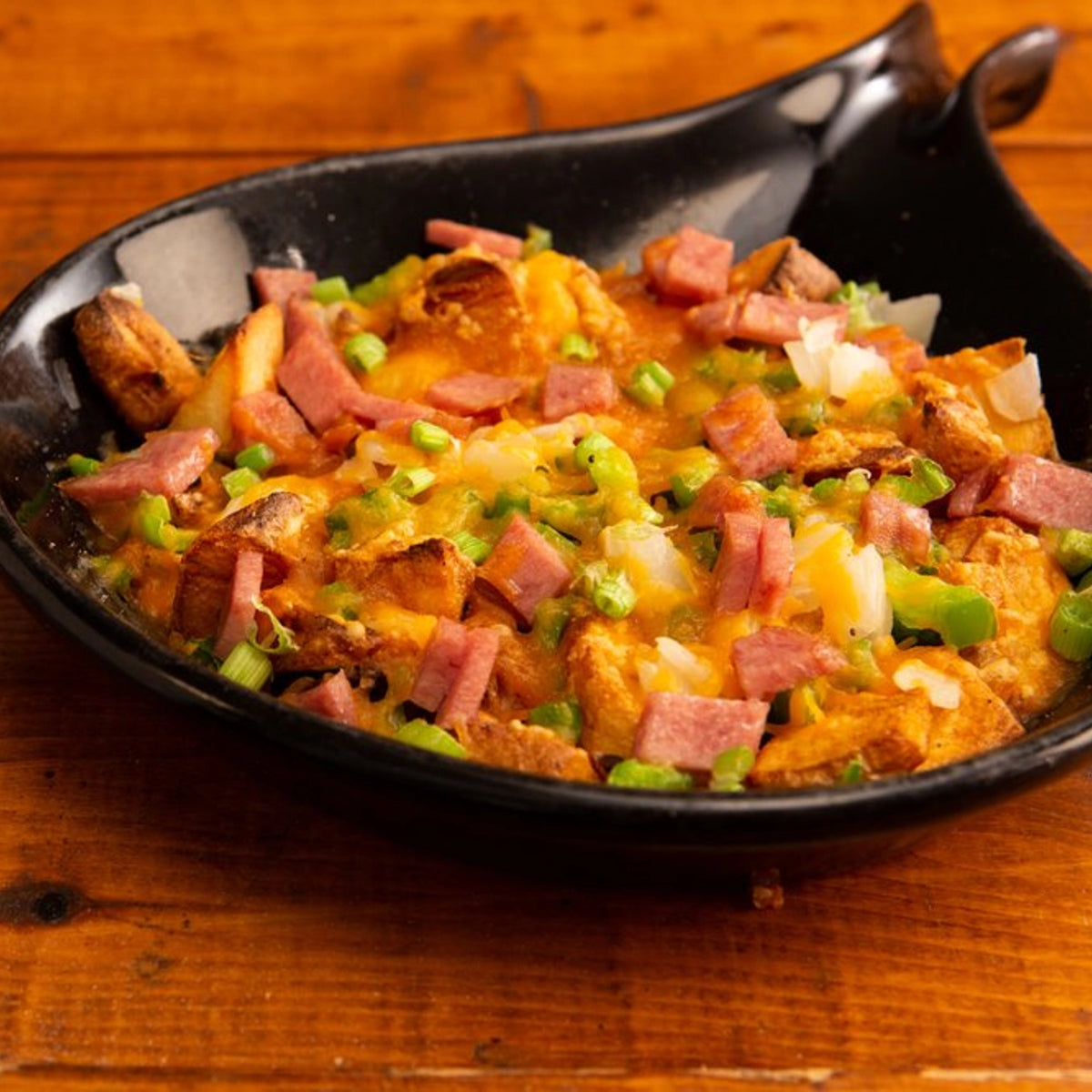 Omelette dish with cheese, ham, and green onions in a black bowl on a wooden surface