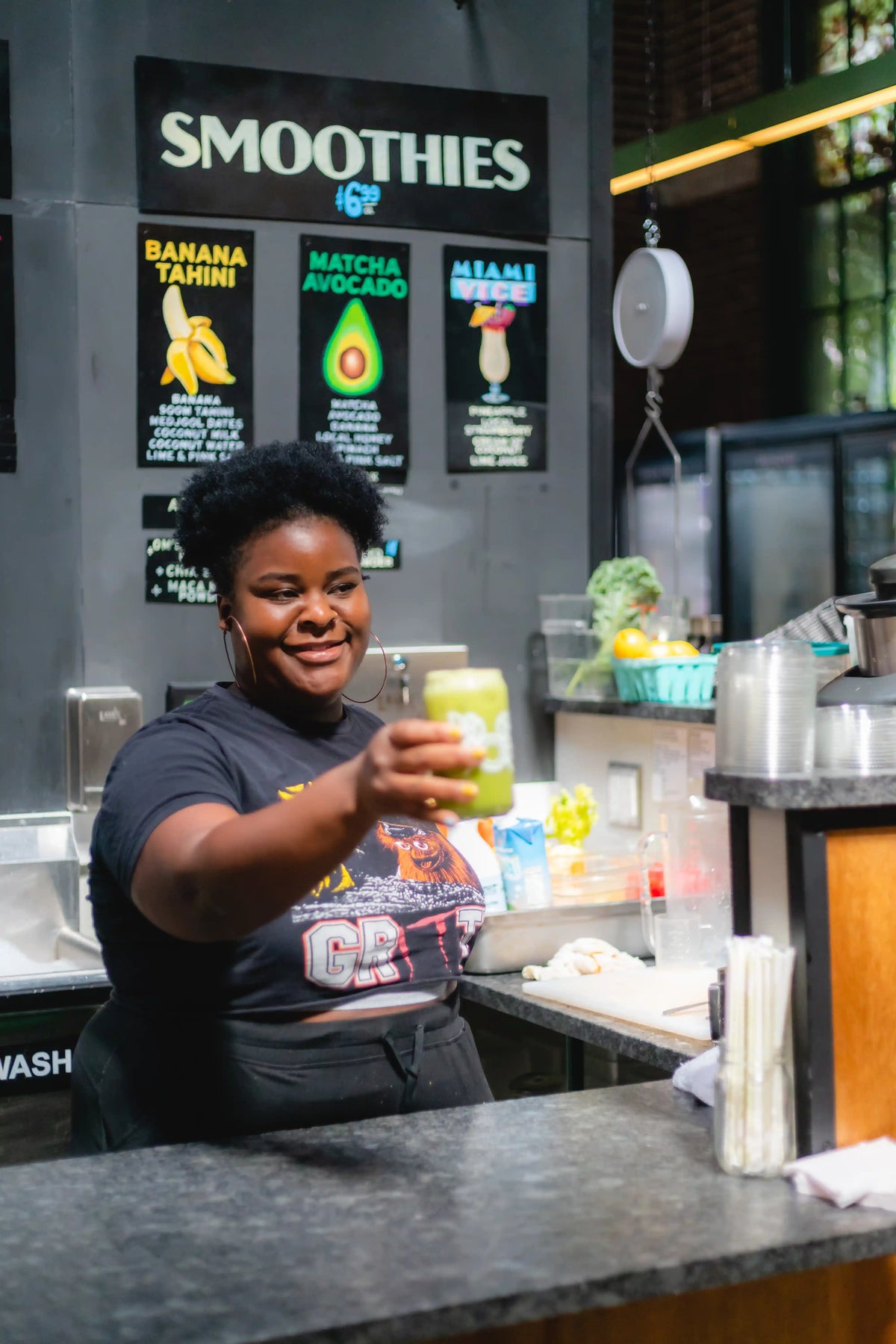 Person holding a smoothie at a smoothie bar with promotional posters on the wall.