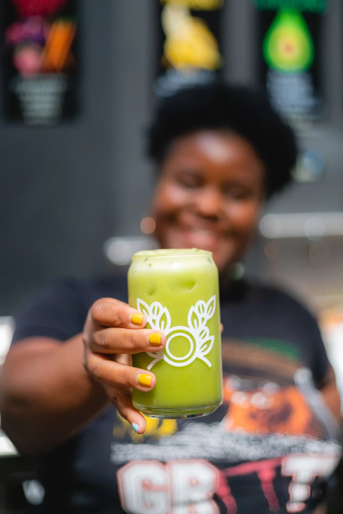 Person holding a green smoothie in a Bean2Bean Coffe Co. branded cup with blurred background