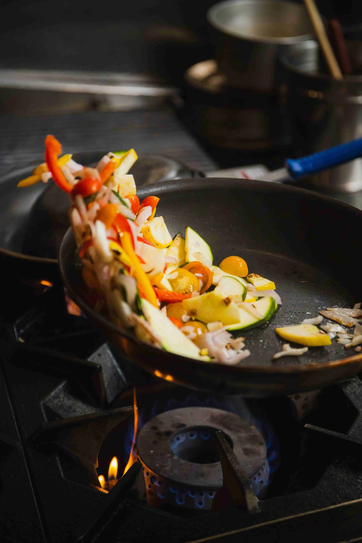 vegetables being sauteed and flipped over a professional kitchen stovetop flame in pan