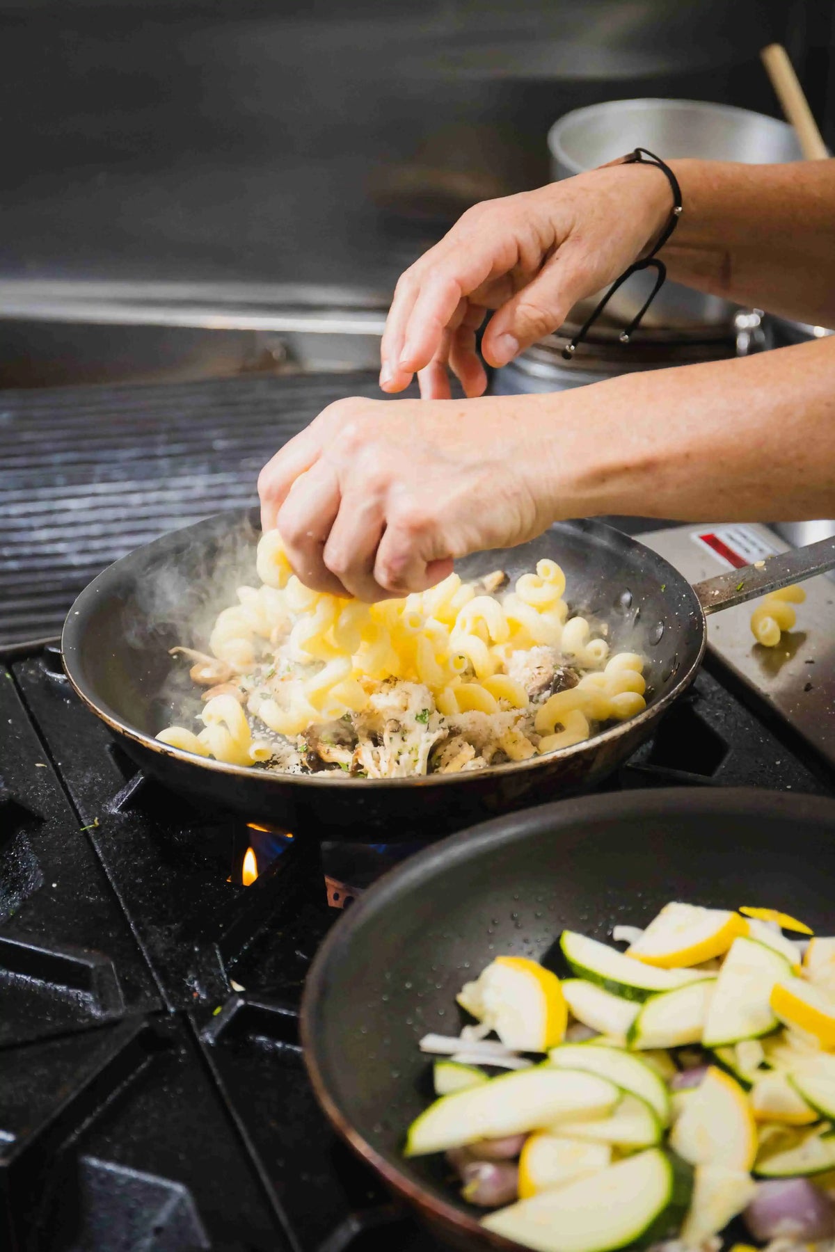 Chef preparing mushroom noodle dish in pan over flame on professional stovetop