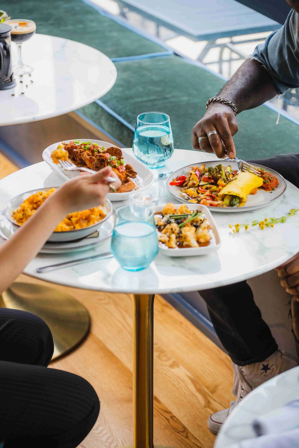 four dishes of food being shared by two people at a small round white table