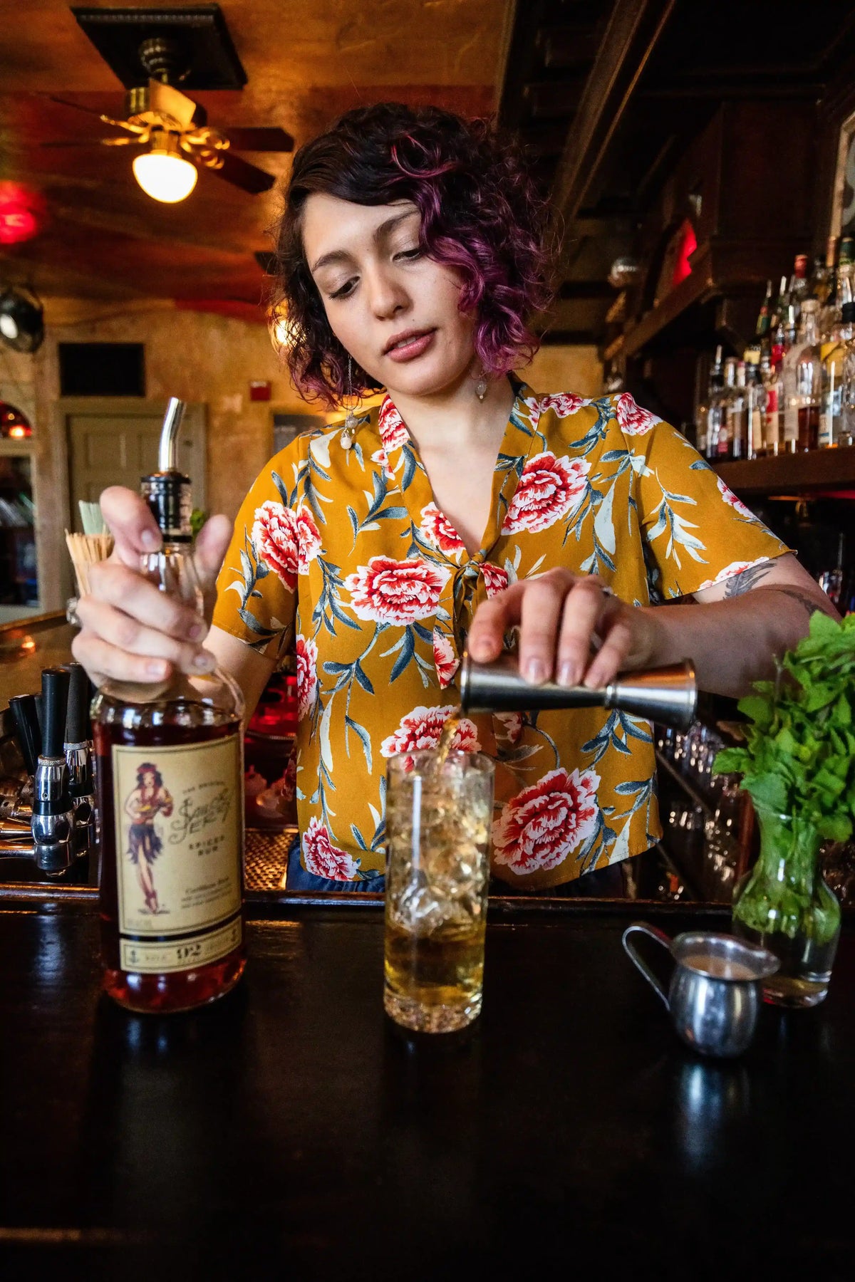 Barista preparing a drink behind the bar with various bottles and glasses.