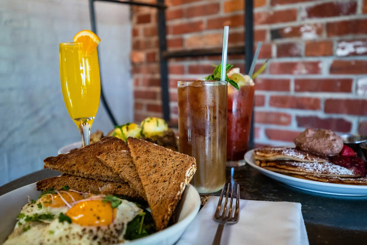 Breakfast setting with toast, eggs, and drinks against a brick wall.