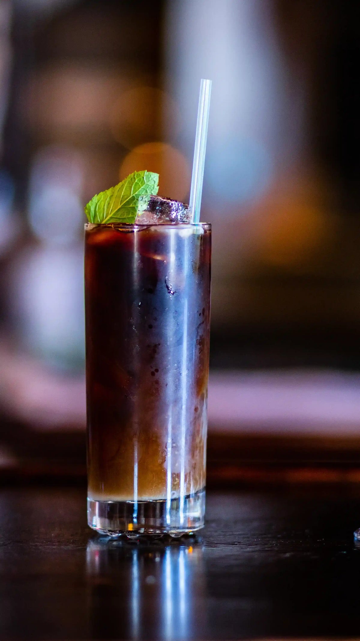 Cold brew coffee cocktail with a mint leaf and straw on a dark surface