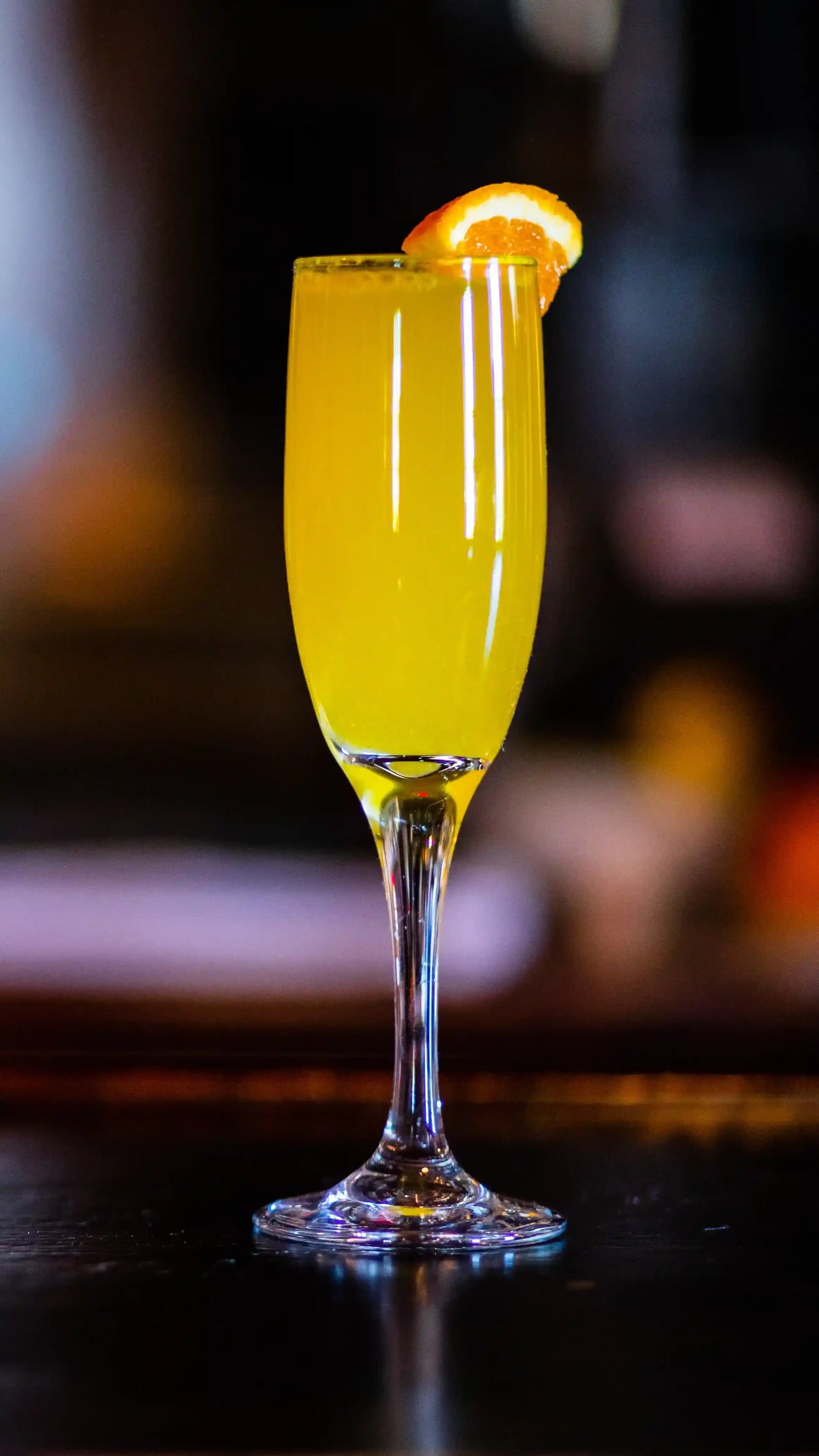 Mimosa cocktail with an orange slice in a flute glass on a dark surface.