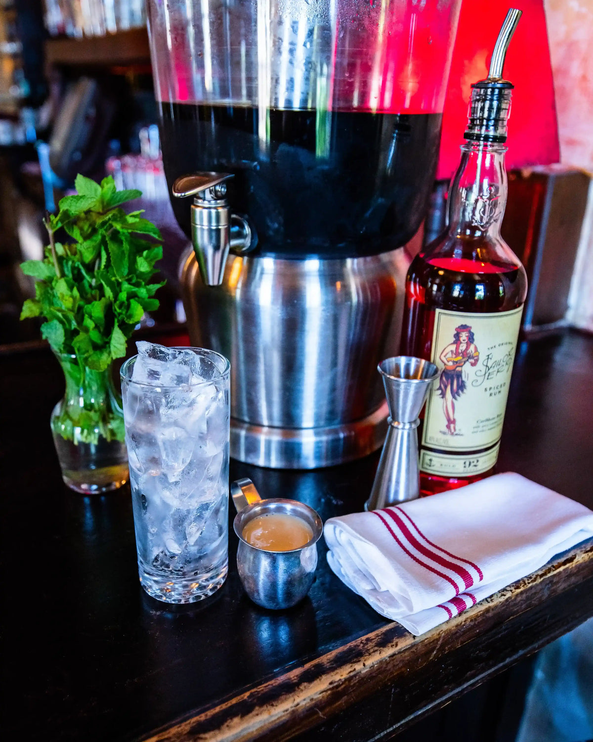 Bar setup with cocktail shaker, bottle, glass with ice, and bar tools on a wooden surface.