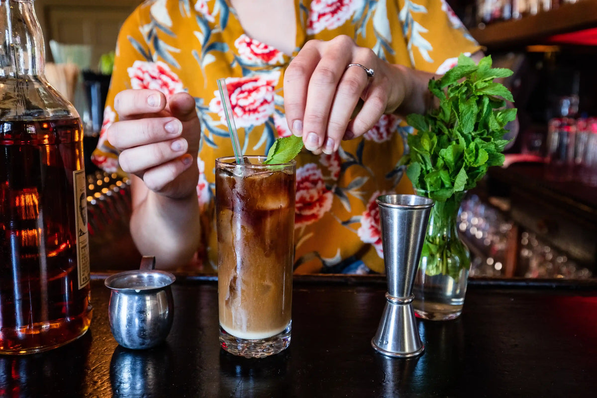 Person preparing a cocktail with ice and mint leaves on a bar counter.