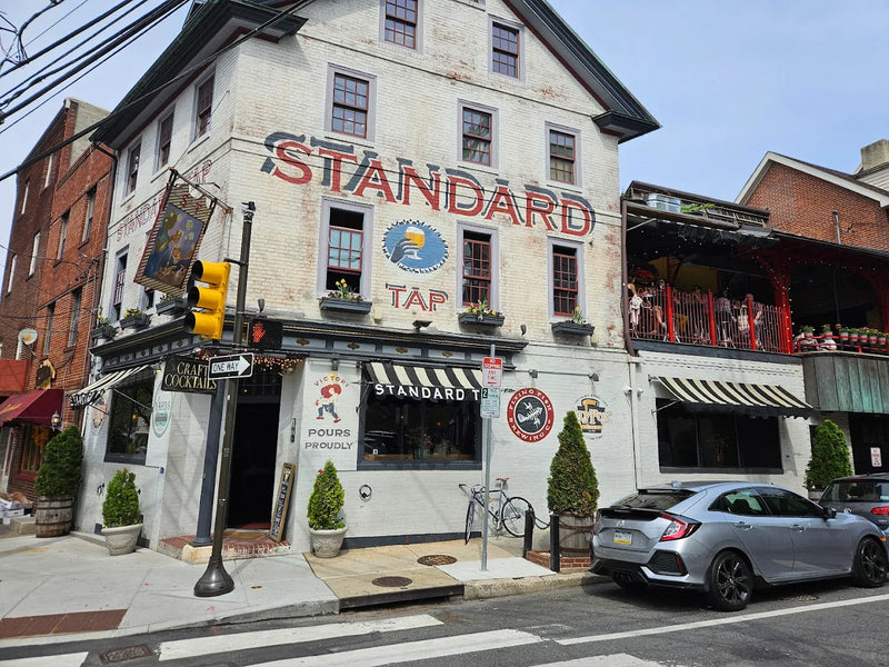 Outside of Standard Tap Bar from opposite corner of street. white brick building with striped awnings