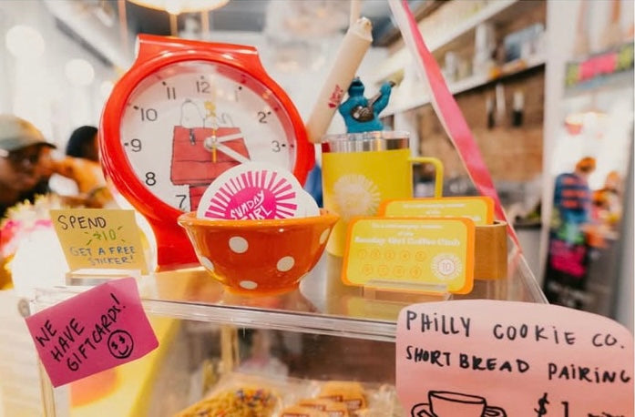 Display of kitchen items including a red clock, bowl, and signs in a store setting.