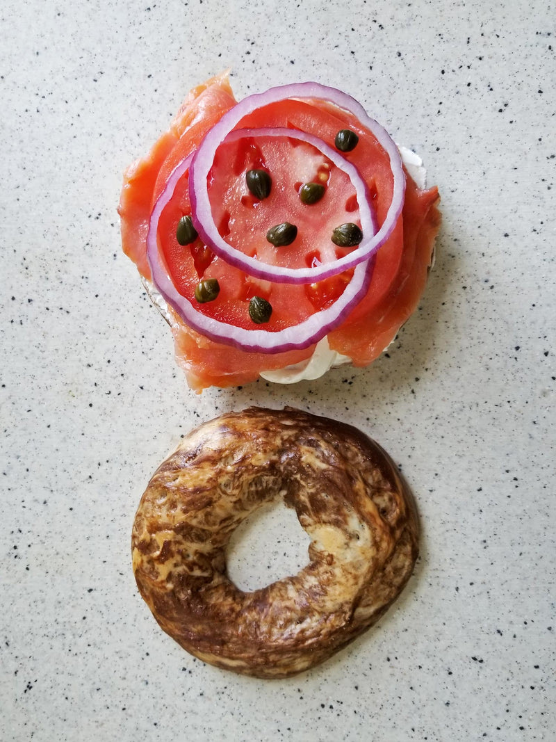 Bagel with smoked salmon, cream cheese, and sliced watermelon on a speckled surface