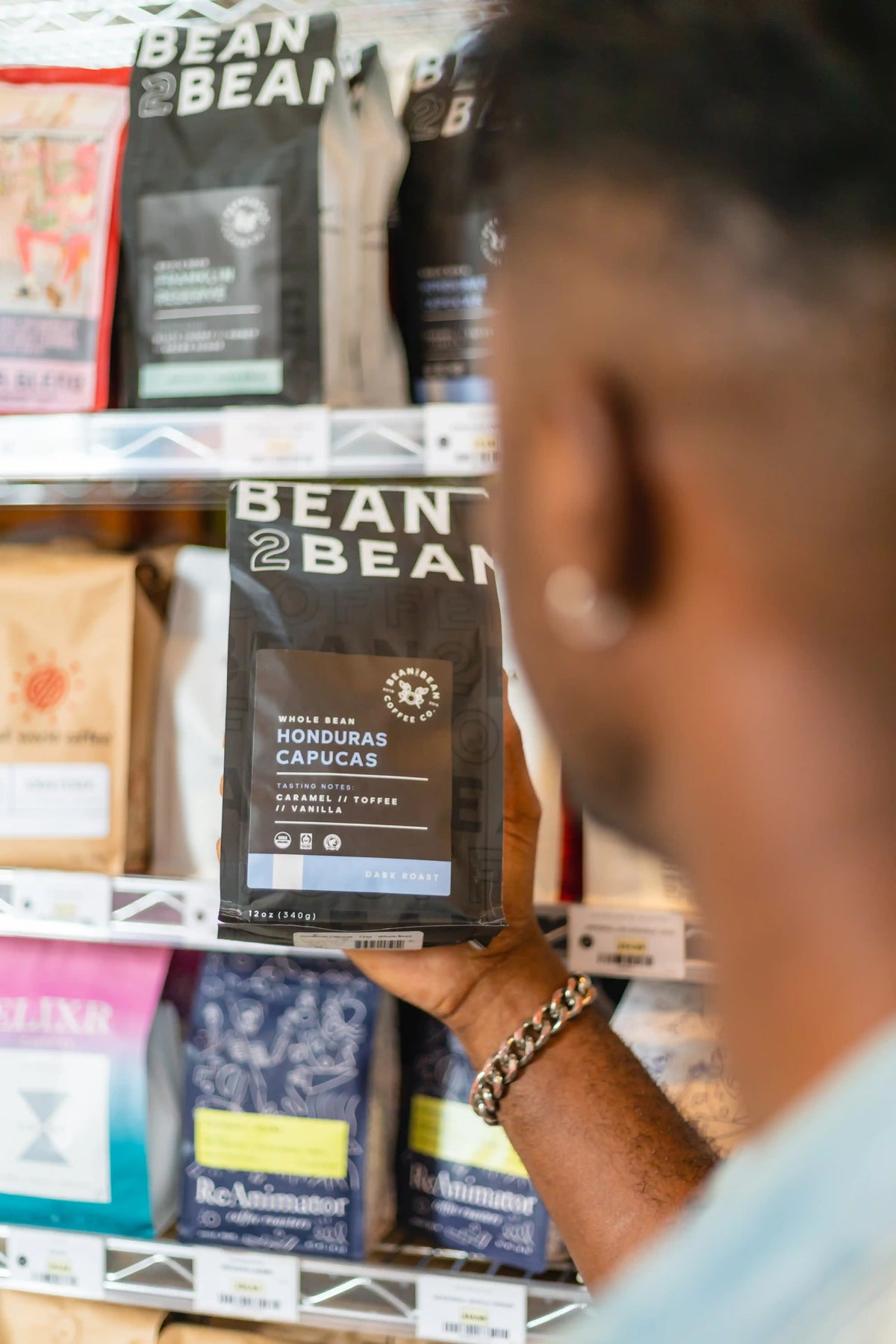 Person selecting a Bean2Bean coffee bag from a shelf in Riverwards Produce store