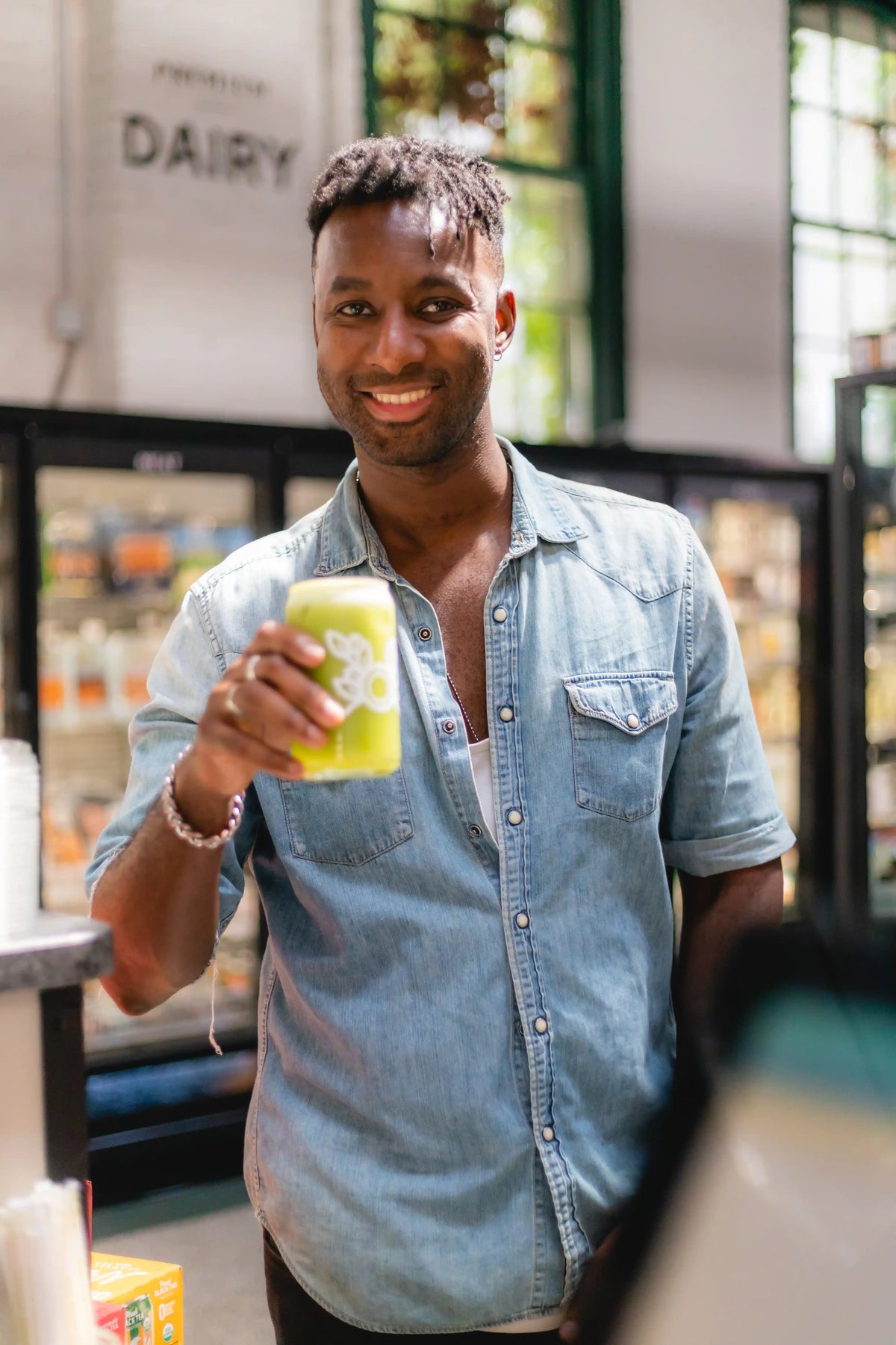Man holding a green smoothie in a Bean2Bean beercan glass inside Riverwards Produce store
