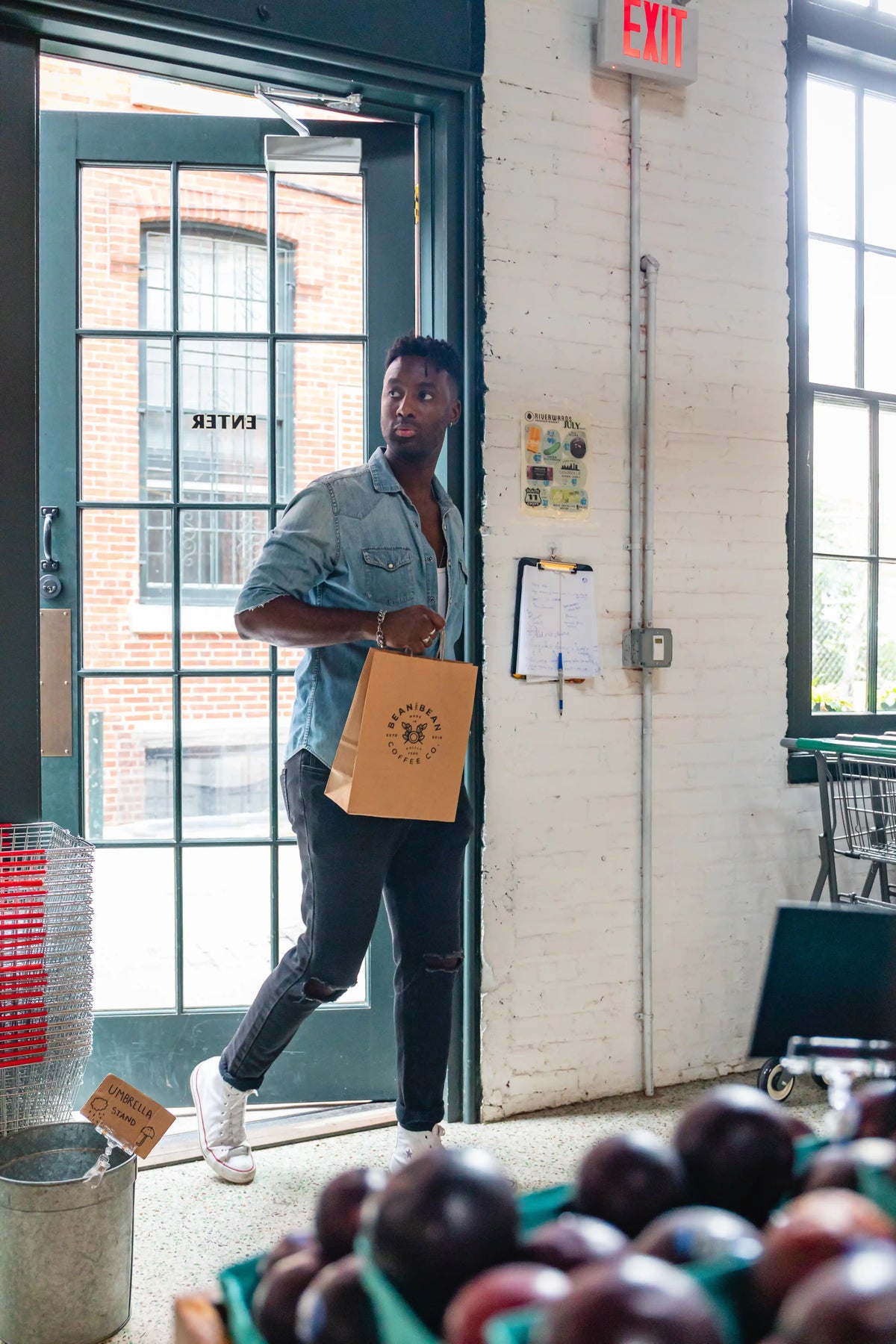 Man holding a brown paper bag in front of a door with a brick wall background