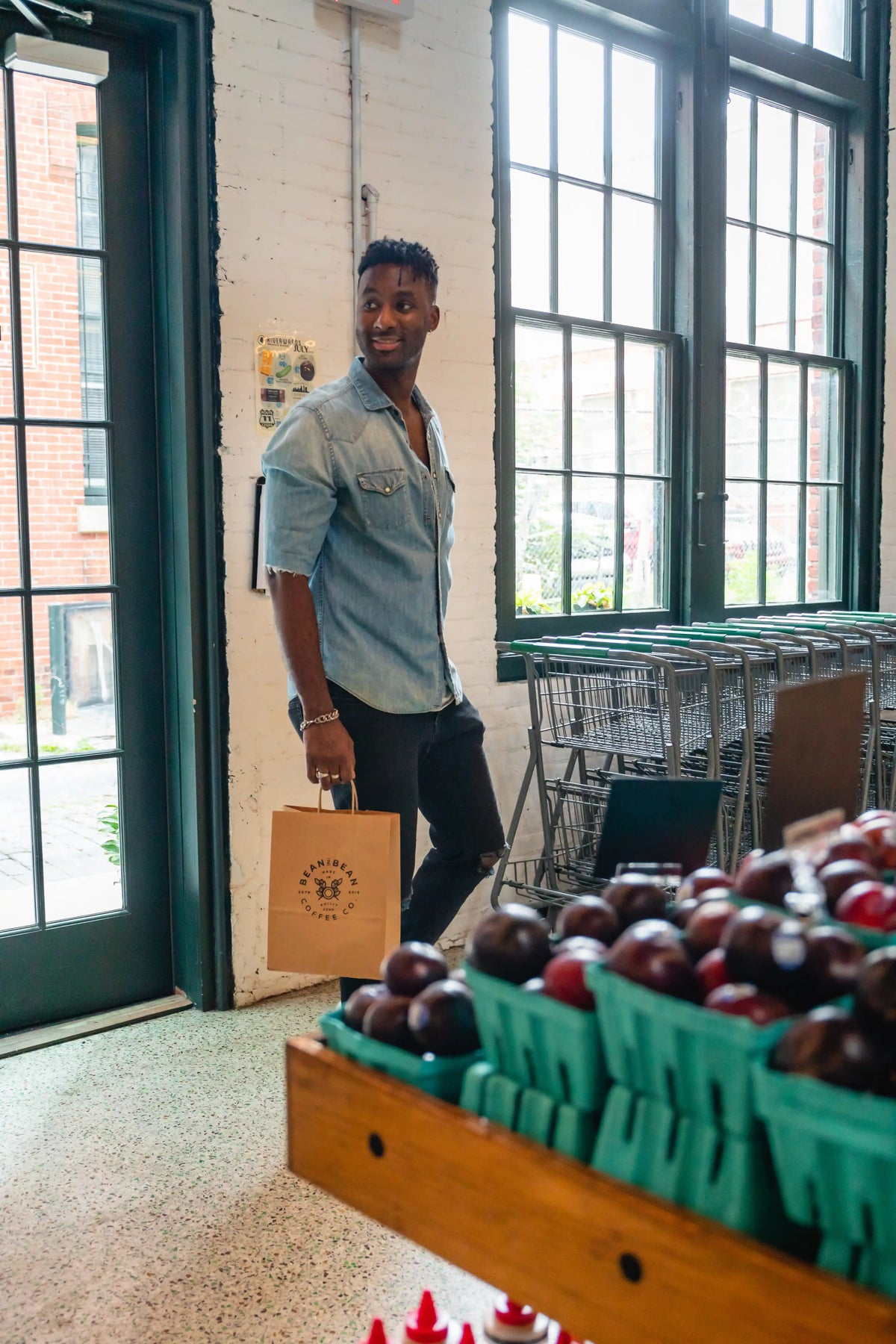 Man walking past a display of fruits and vegetables in a store.