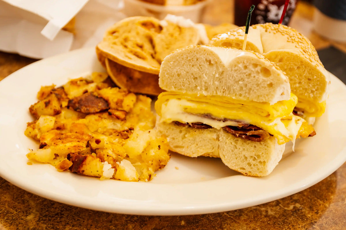 Breakfast sandwich with egg and cheese on a bun, served with hash browns on a white plate.