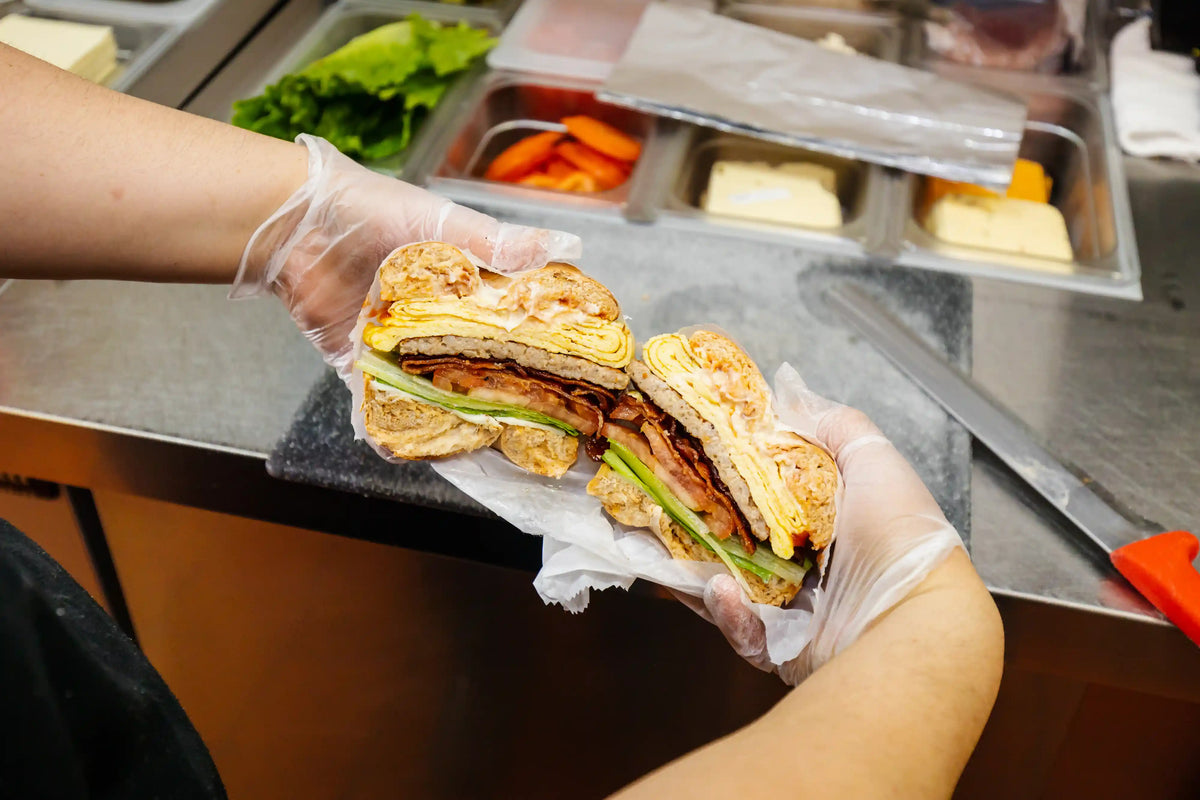 Person holding a sandwich cut in half with visible ingredients in a kitchen setting.