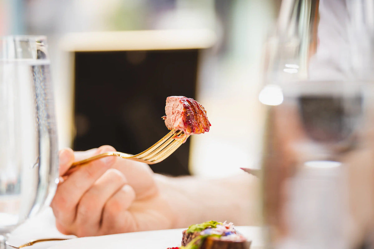 Person holding a fork with a piece of meat over a plate of food in a restaurant setting.