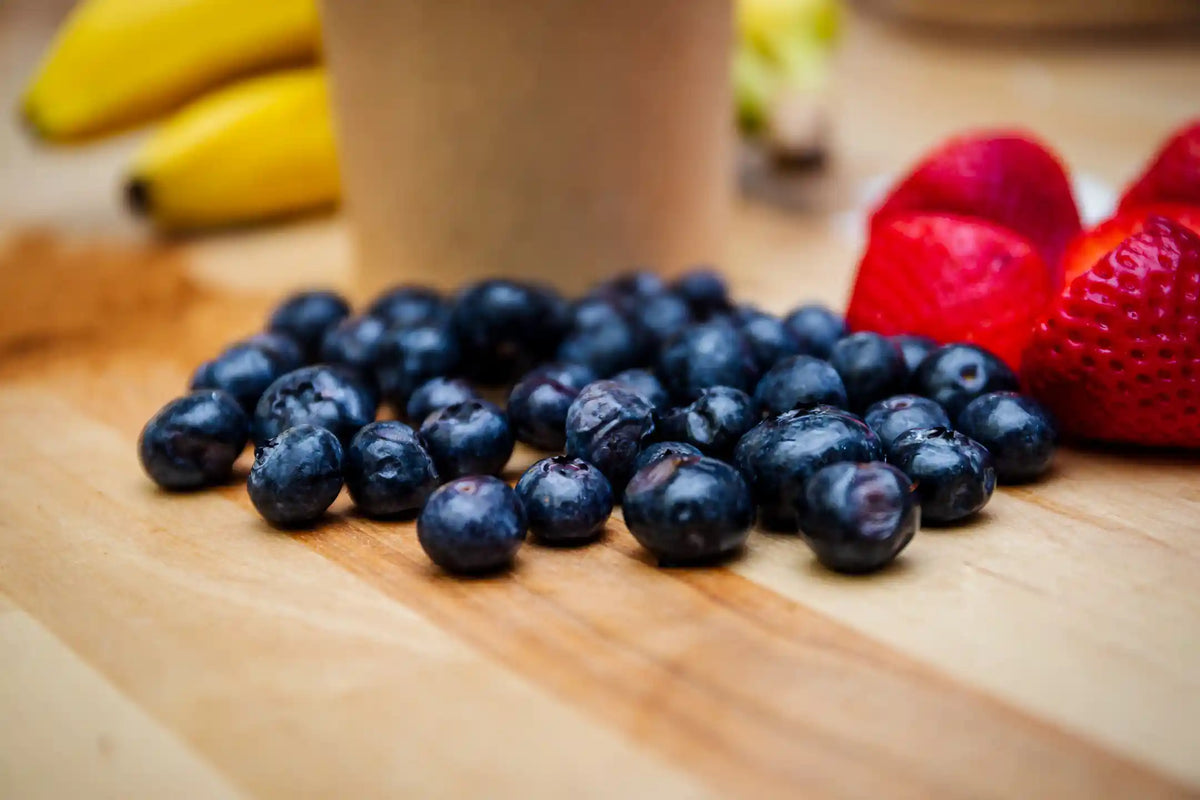 Blueberries on a wooden surface with strawberries and bananas in the background
