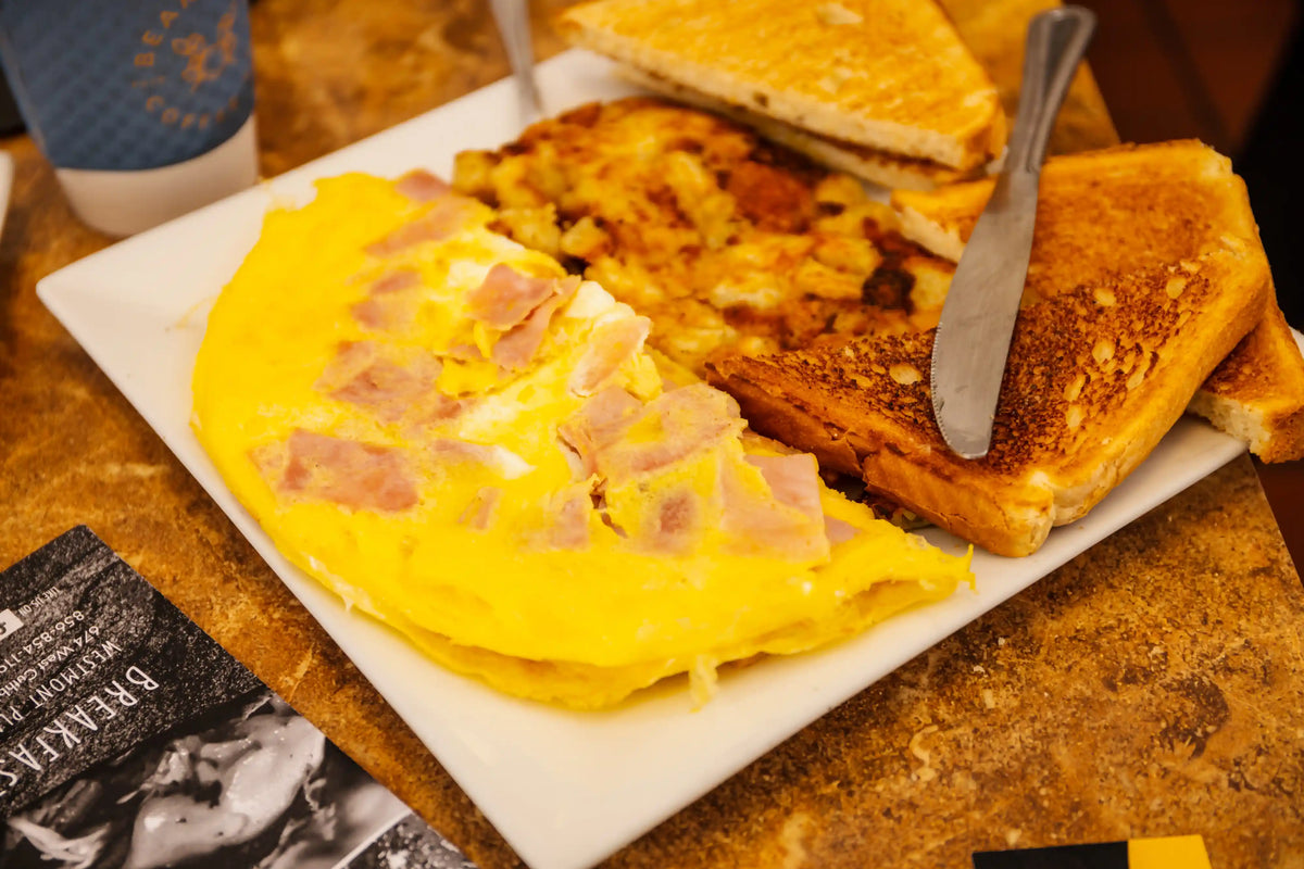 Omelette with ham and toast on a white plate with a cup and napkin in the background.