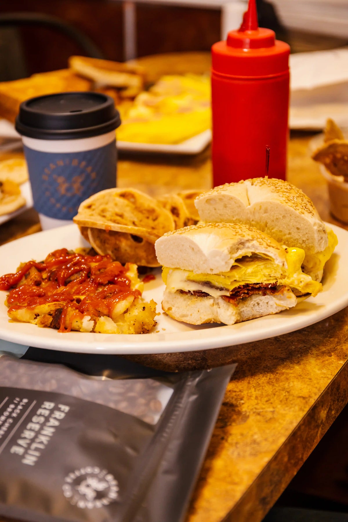 Plate of sandwiches and a side dish on a wooden table with a ketchup bottle in the background.