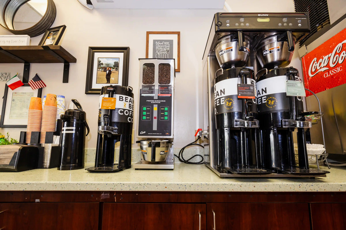 Coffee dispensers on a counter with a Coca-Cola sign in the background