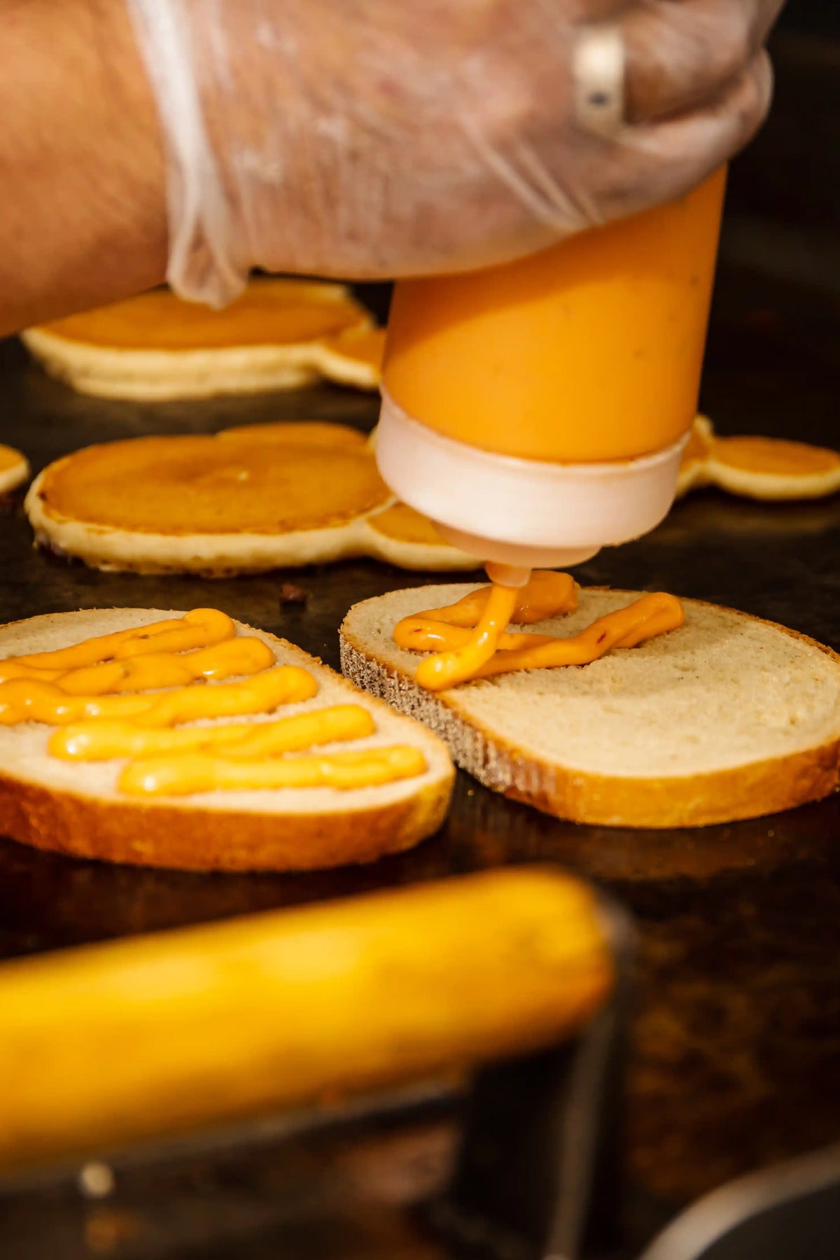 Person spreading yellow condiment on bread slices with a squeeze bottle.