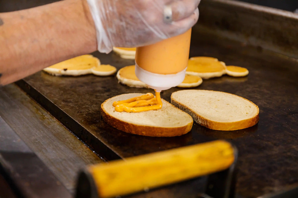 Person spreading yellow condiment on a slice of bread using a small container.